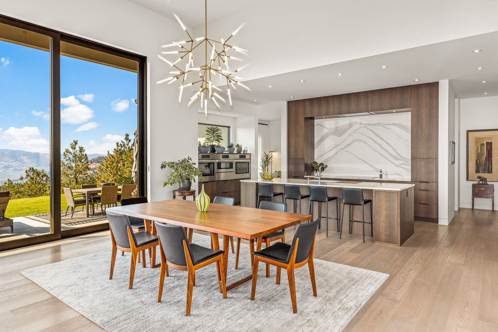 Dining room under a sculptural chandelier, with the kitchen and a valley view beyond